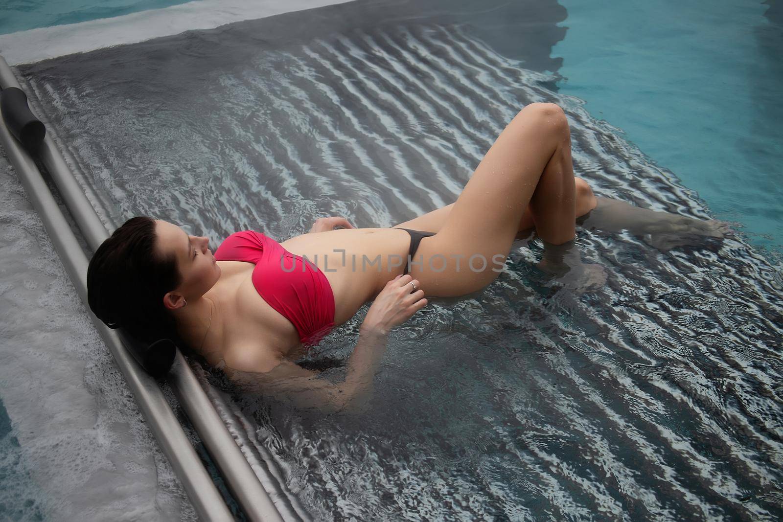 High angle of slim barefoot woman in red swimwear lying on grates in clean water of pool on resort