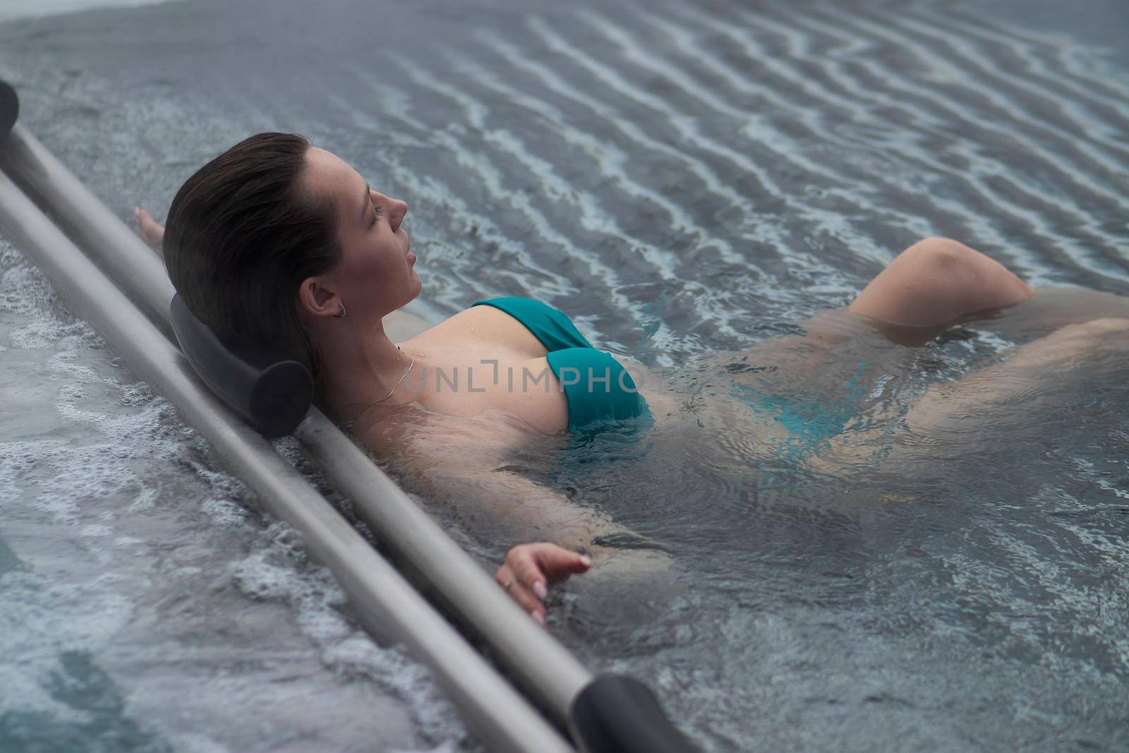 High angle of slim barefoot woman in red swimwear lying on grates in clean water of pool on resort