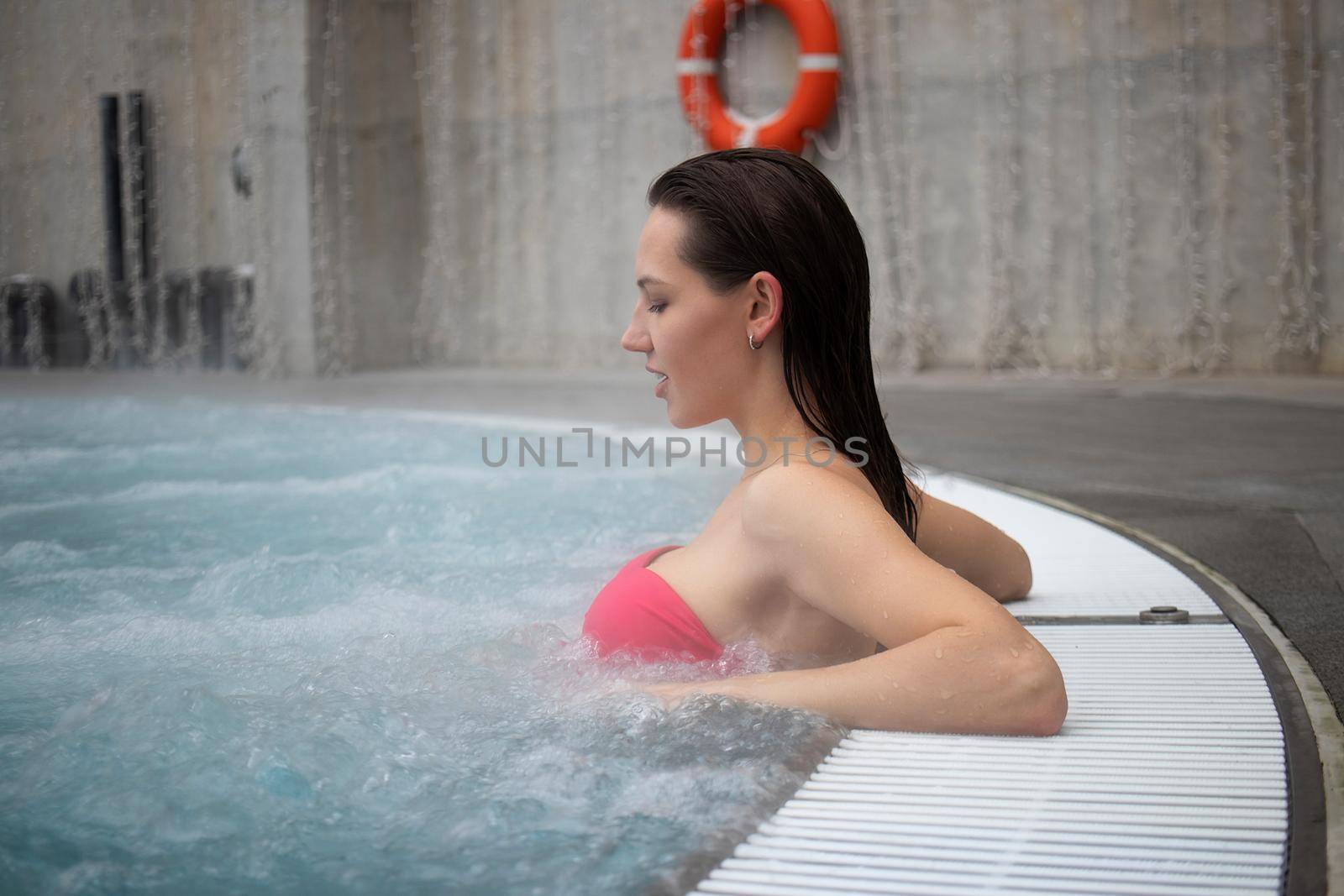 Seductive woman in pink bra crossing arms and looking away while resting in clean water of hot spring on resort