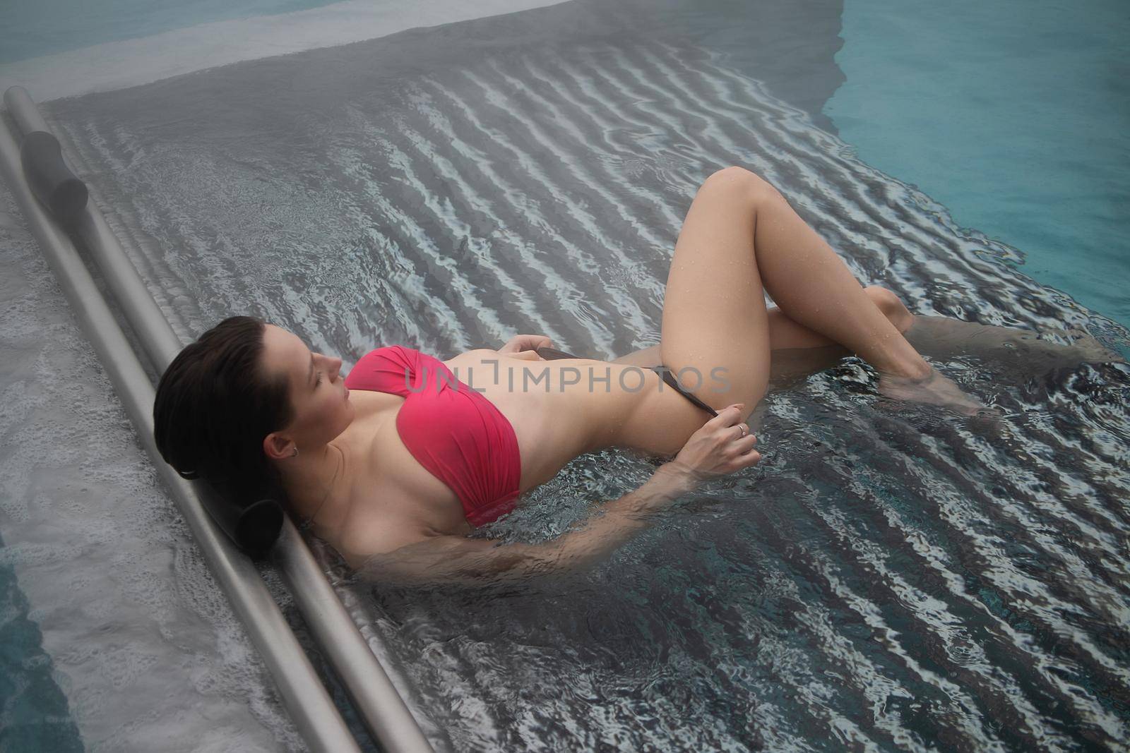 High angle of slim barefoot woman in red swimwear lying on grates in clean water of pool on resort