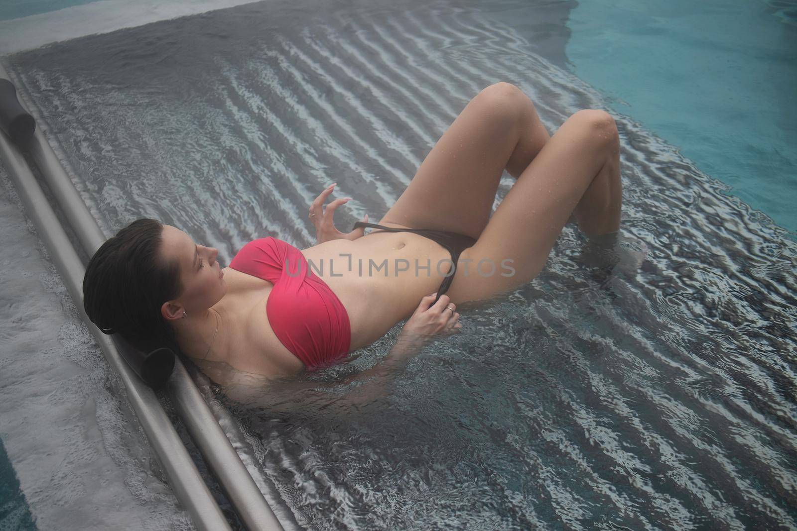 High angle of slim barefoot woman in red swimwear lying on grates in clean water of pool on resort