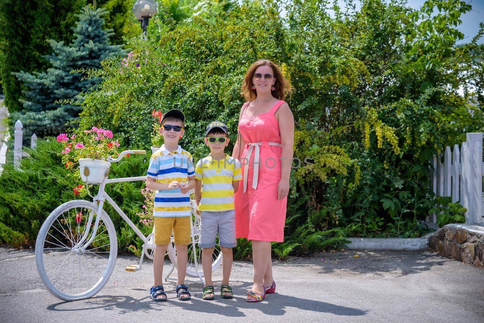 Portrait of happy family mother and two boys near bicycle with flowers on it. kids standing warm sunny weather, leisure time with family