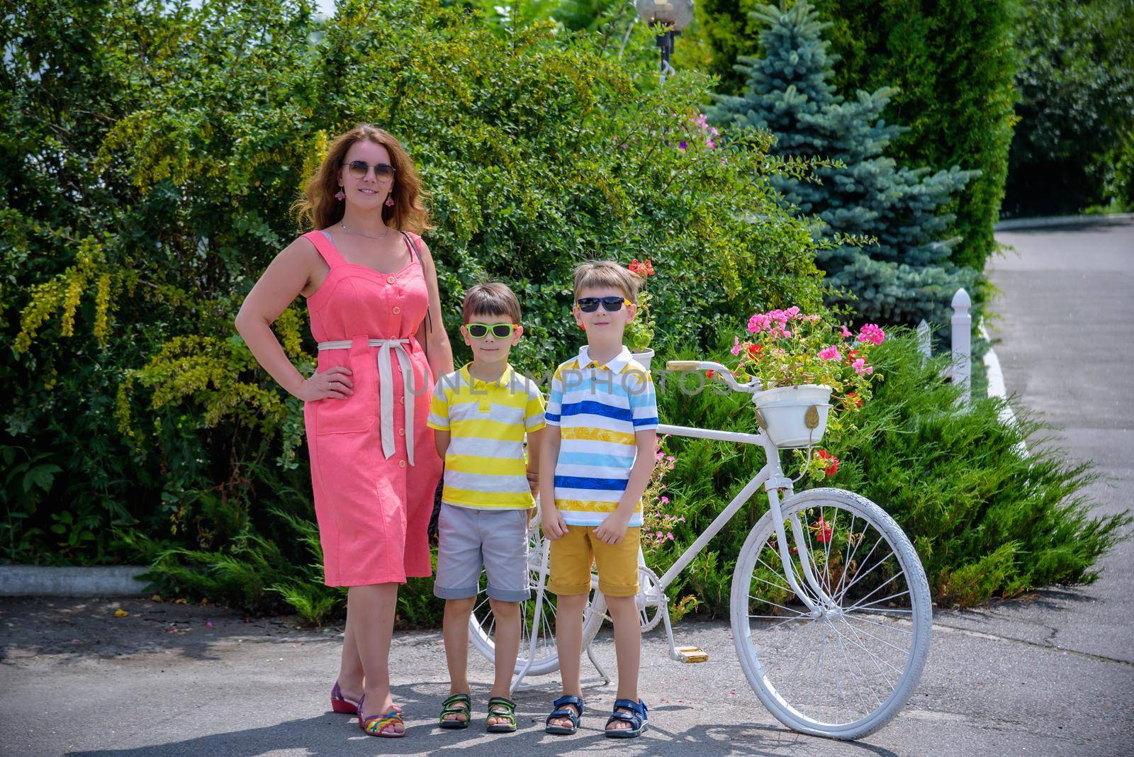 Portrait of happy family mother and two boys near bicycle with flowers on it. kids standing warm sunny weather, leisure time with family. by Kobysh