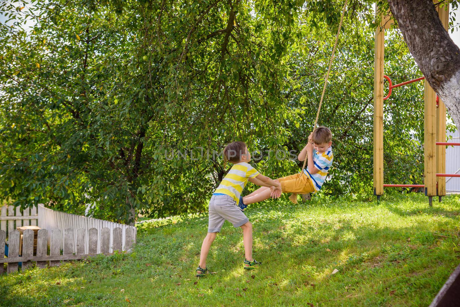 Two adorable happy little boys is having fun on a rope swing which he has found while having rest outside city. Active leisure time with children by Kobysh