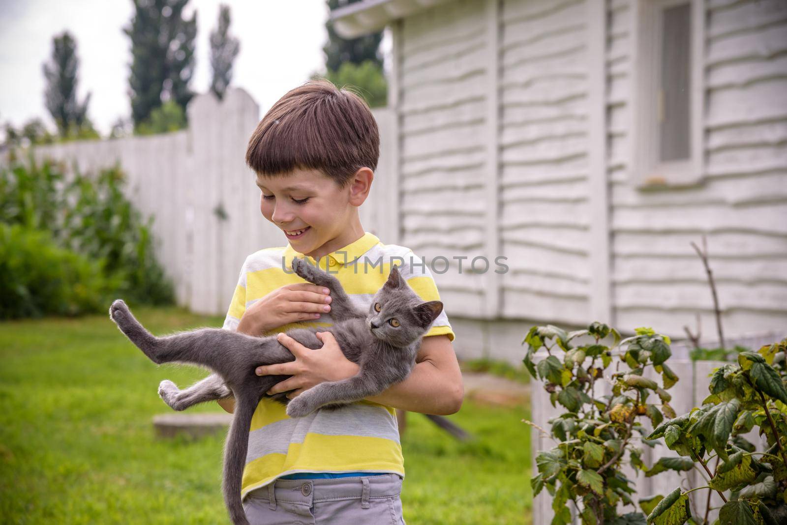 Funny boy hugging a cat with lots of love. Portrait of child holding on hands a Kitten. Playing with a cat on village countryside.