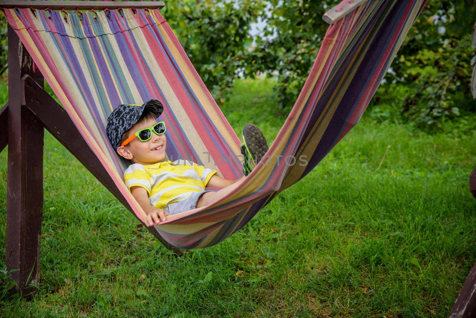 Cute little Caucasian boy relaxing and having fun in multicolored hammock in backyard or outdoor playground. Summer active leisure for kids. Child swinging on hammock. Activities for children.