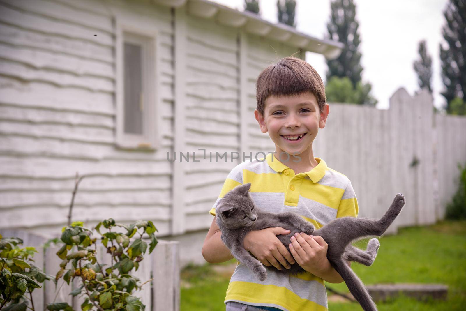 Funny boy hugging a cat with lots of love. Portrait of child holding on hands a Kitten. Playing with a cat on village countryside.