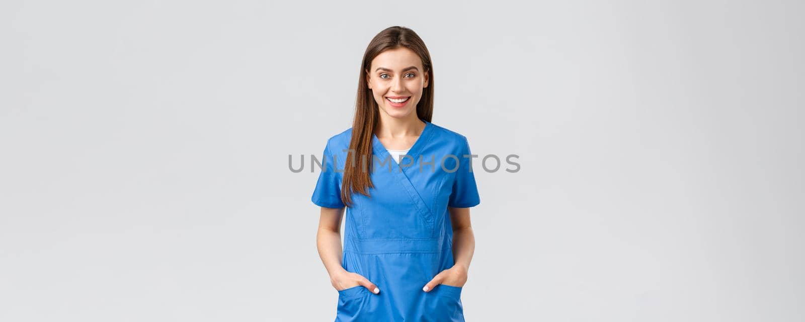 Healthcare workers, prevent virus, insurance and medicine concept. Cheerful smiling beautiful doctor, female nurse in blue scrubs, intern in hospital staying positive, standing grey background.