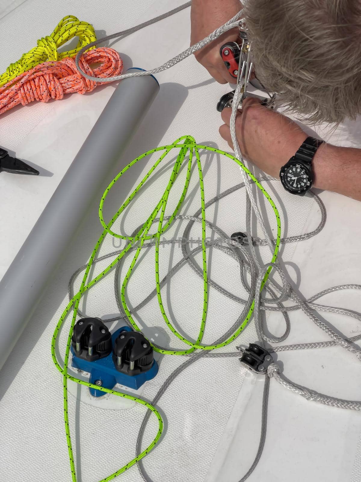 Close-up view of a sailor sets up a sports boat, set of ship equipment, ropes for management of the sailboat of different color, pulleys and ropes, yachting sport, rollers, levers, carbines by vladimirdrozdin