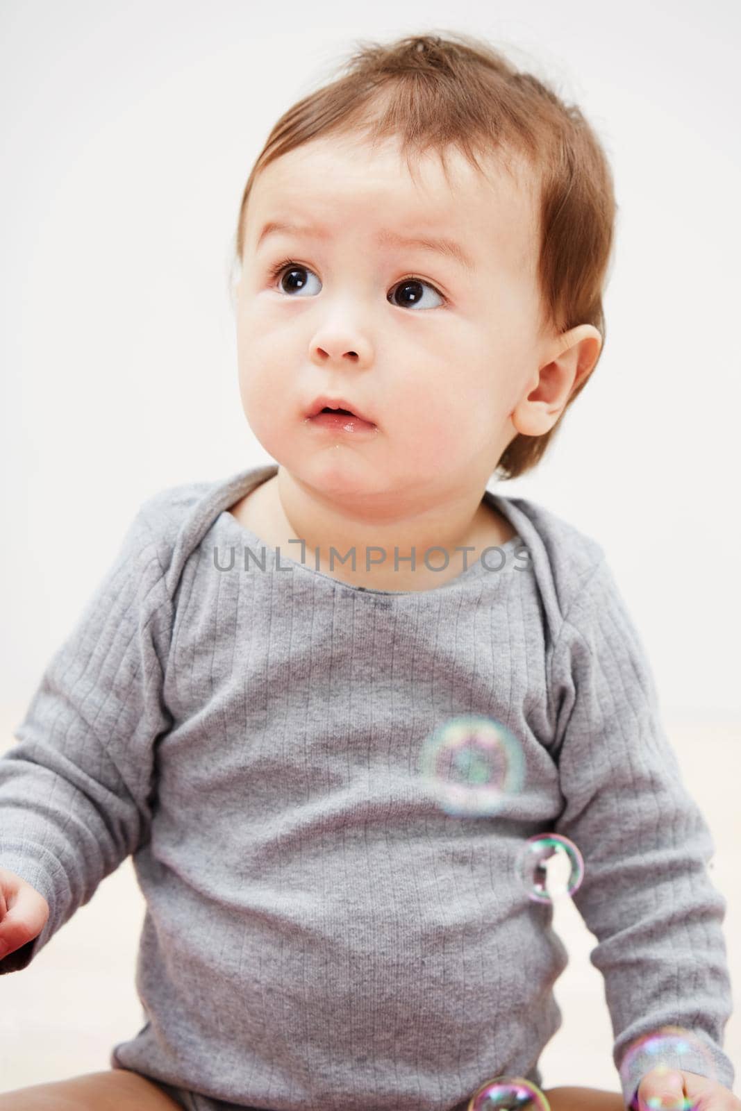 Shot of an adorable baby boy looking at bubbles floating in the air around him.