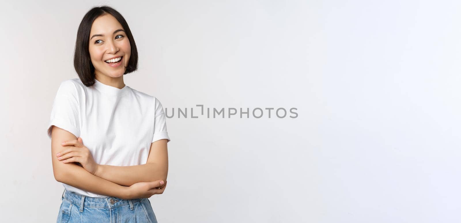 Portrait of happy asian woman smiling, posing confident, cross arms on chest, standing against studio background by Benzoix