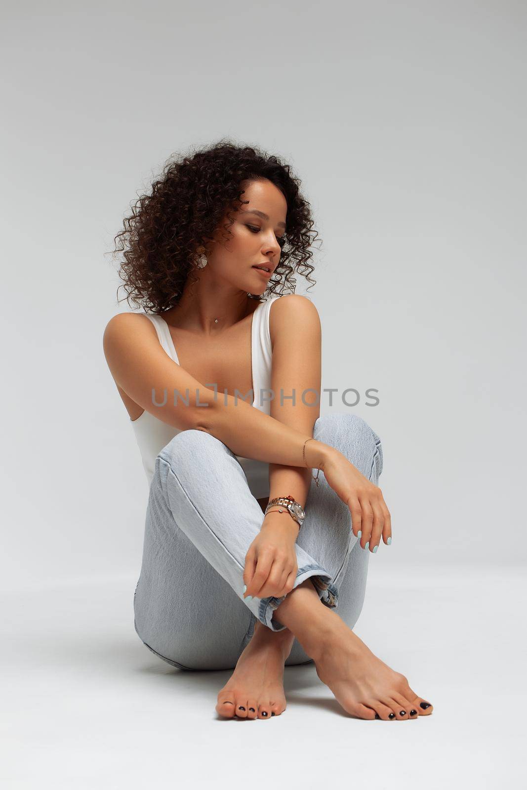 Full body of confident young barefoot female model with curly hairstyle wearing trendy denim jacket and jeans