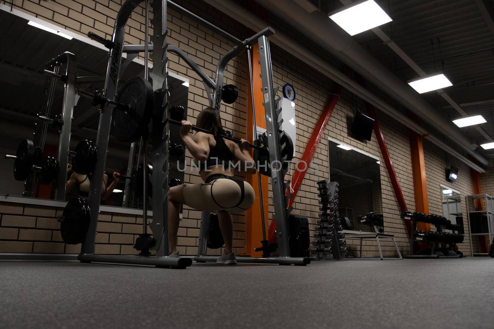 Fit woman squatting with barbell in gym by 3KStudio