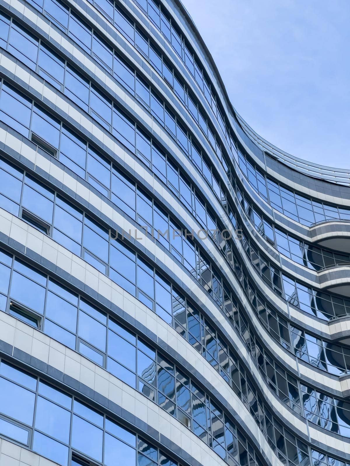 Curved lines of the facade of a large building, reflection of the blue sky in the glass walls, conceptual design. High quality photo