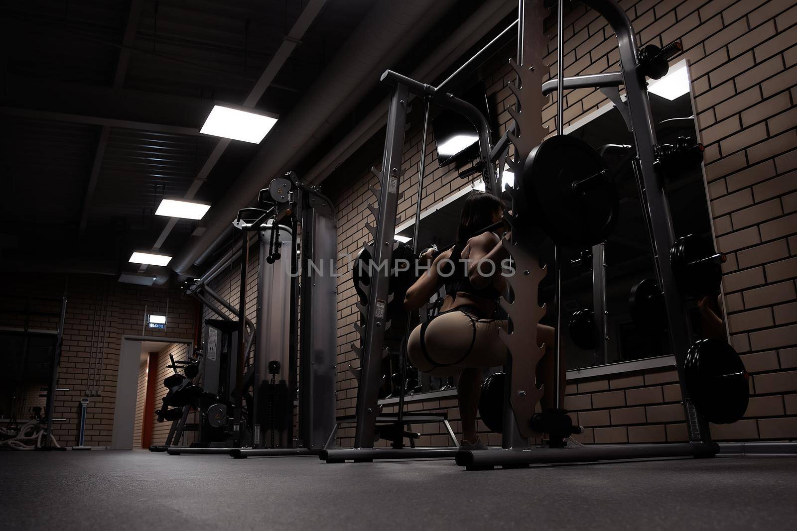 Fit woman squatting with barbell in gym by 3KStudio