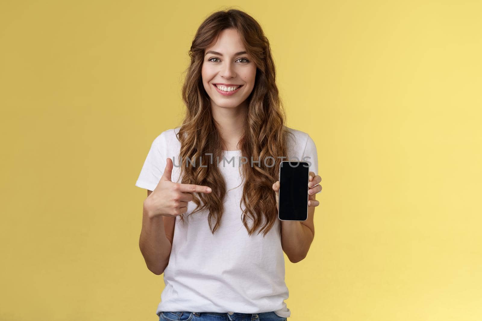 Girl have everything need smartphone. Cheerful relaxed carefree woman long curly hairstyle hold mobile phone pointing forefinger cellphone smiling broadly explain how app works yellow background by Benzoix