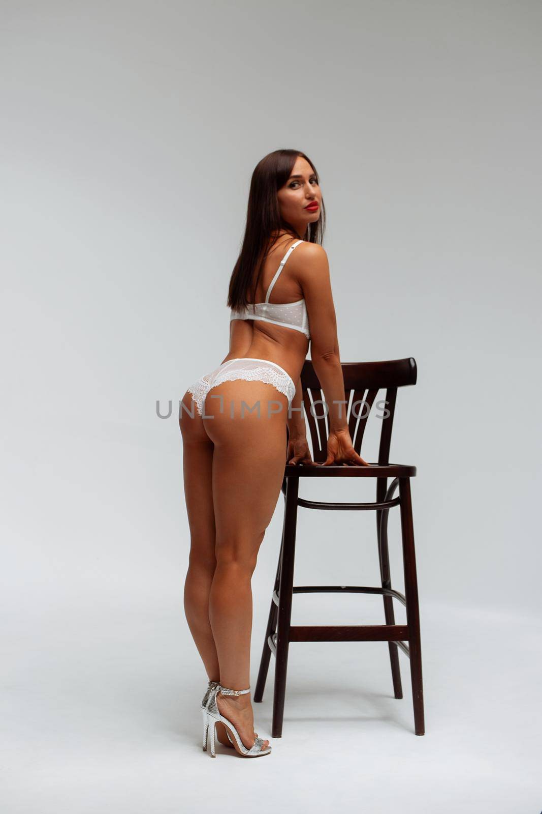 Confident female wearing white underwear standing with hands on waist on white background and looking at camera