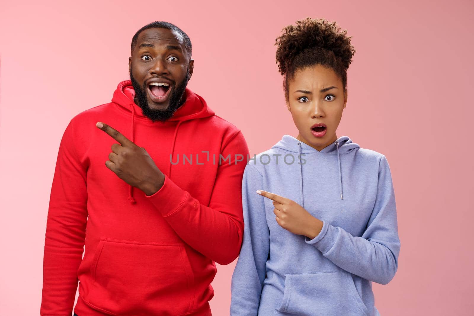 Girlfriend shocked boyfriend friends made surprise party look frustated displeased pointing upper left corner man feeling amazed thankful smiling delighted standing pink background.