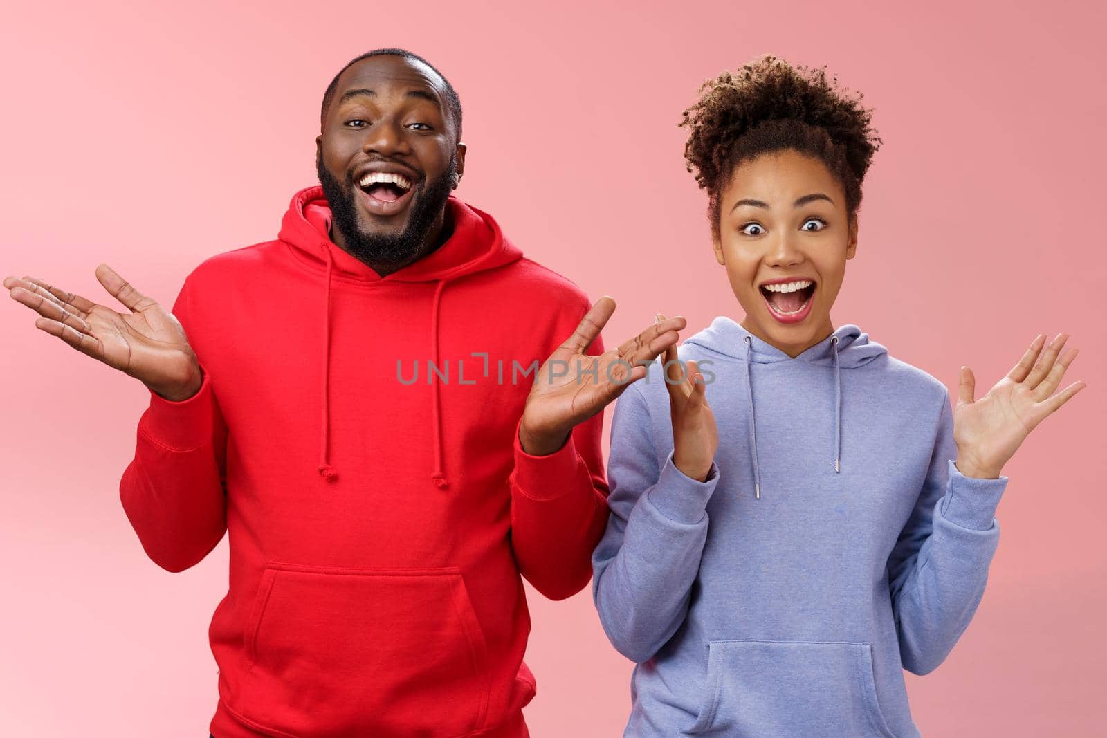 Guys receive nice surprise. Two attractive carefree surprised happy african man woman clapping hands joyfully greeting welcoming guests inviting people joing party standing friendly pink background by Benzoix