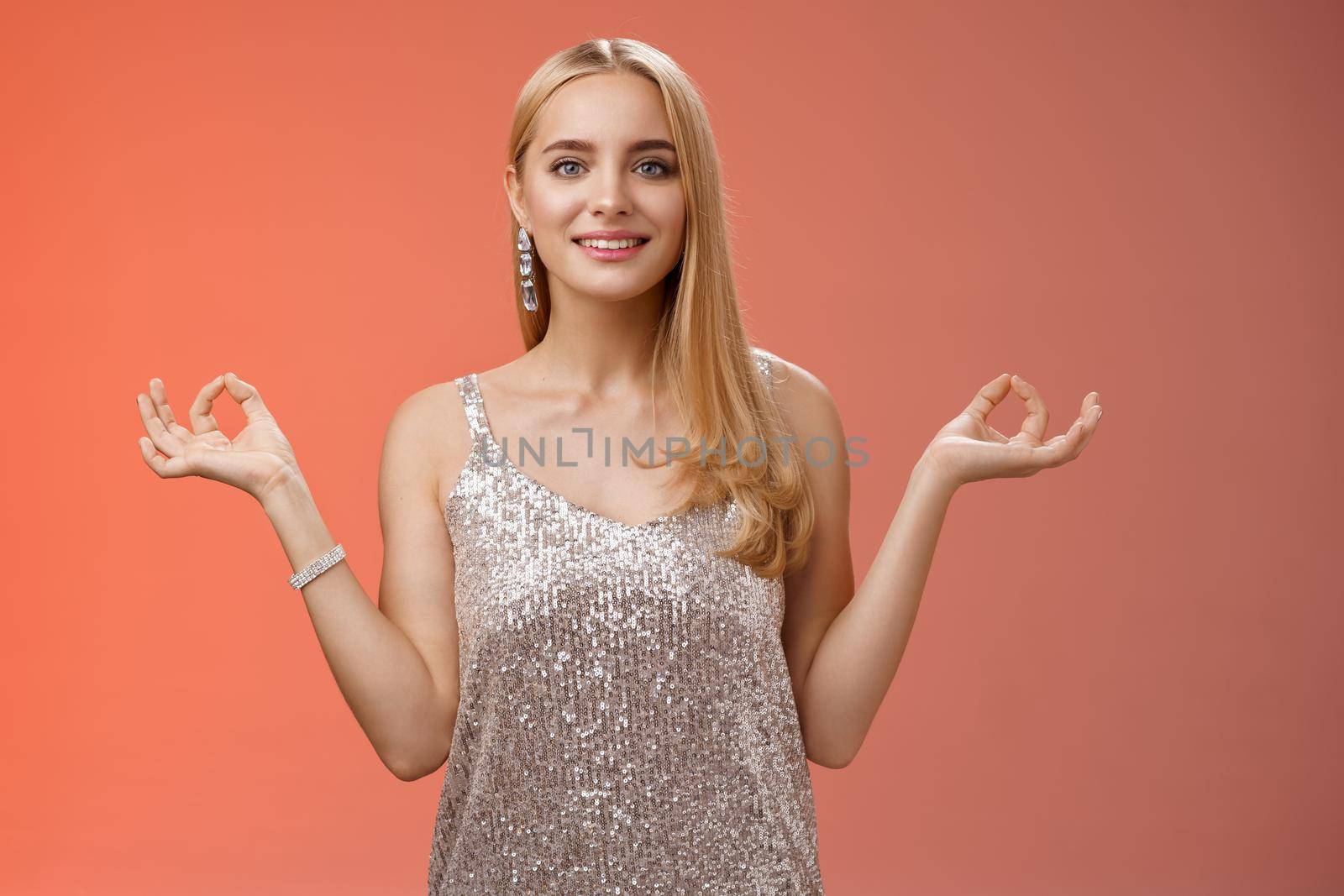 Lifestyle. Calm relieved happy fabulous young blond woman in silver stylish luxury dress standing relaxed red background zen lotus pose reach nirvana smiling peaceful carefree meditating breathing practice.