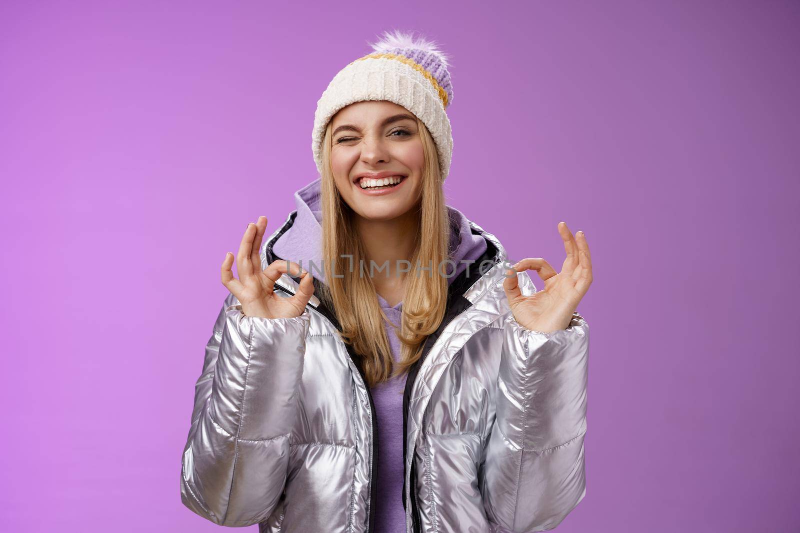 Sassy attractive blond girl in outdoor stylish jacket hat hoodie show no problem okay perfection gesture satisfied good hotel quality smiling broadly winking cheeky camera, enjoying holidays.