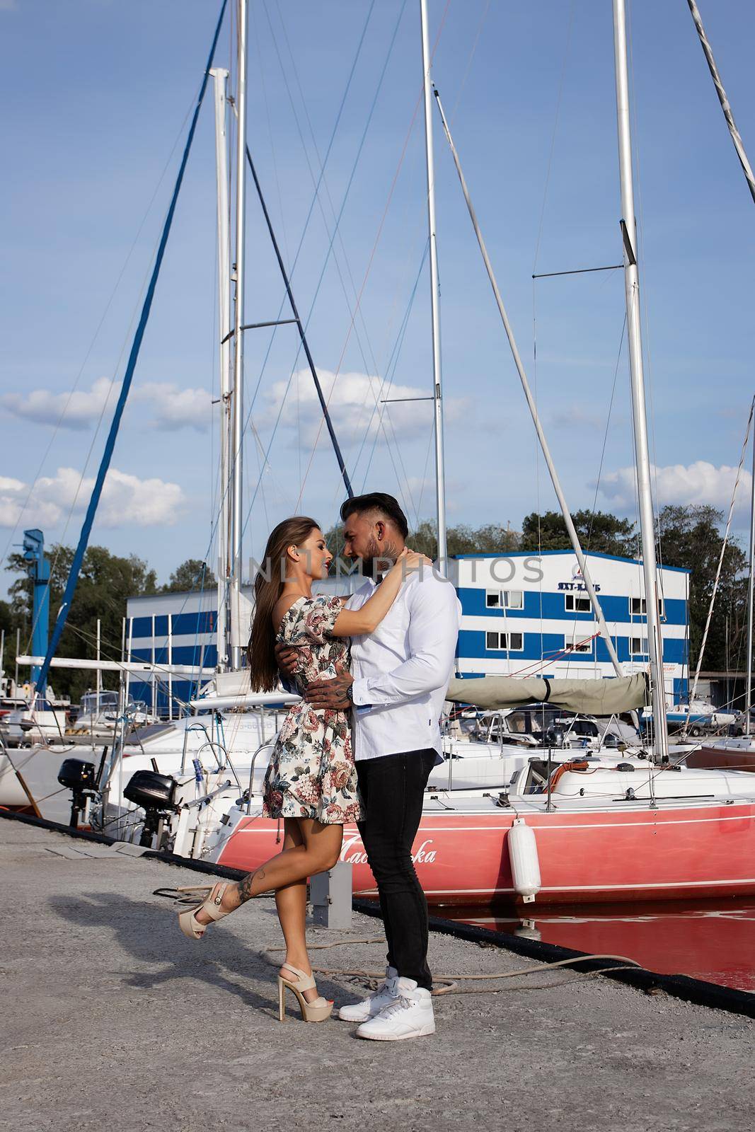 Side view of cheerful couple in love hugging in harbor with boats on sunny day in summer