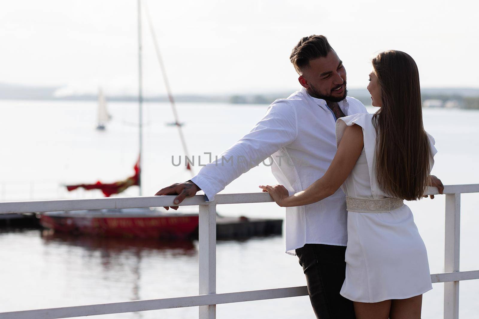 Loving couple hugging while standing on embankment near boats on sunny day in summer