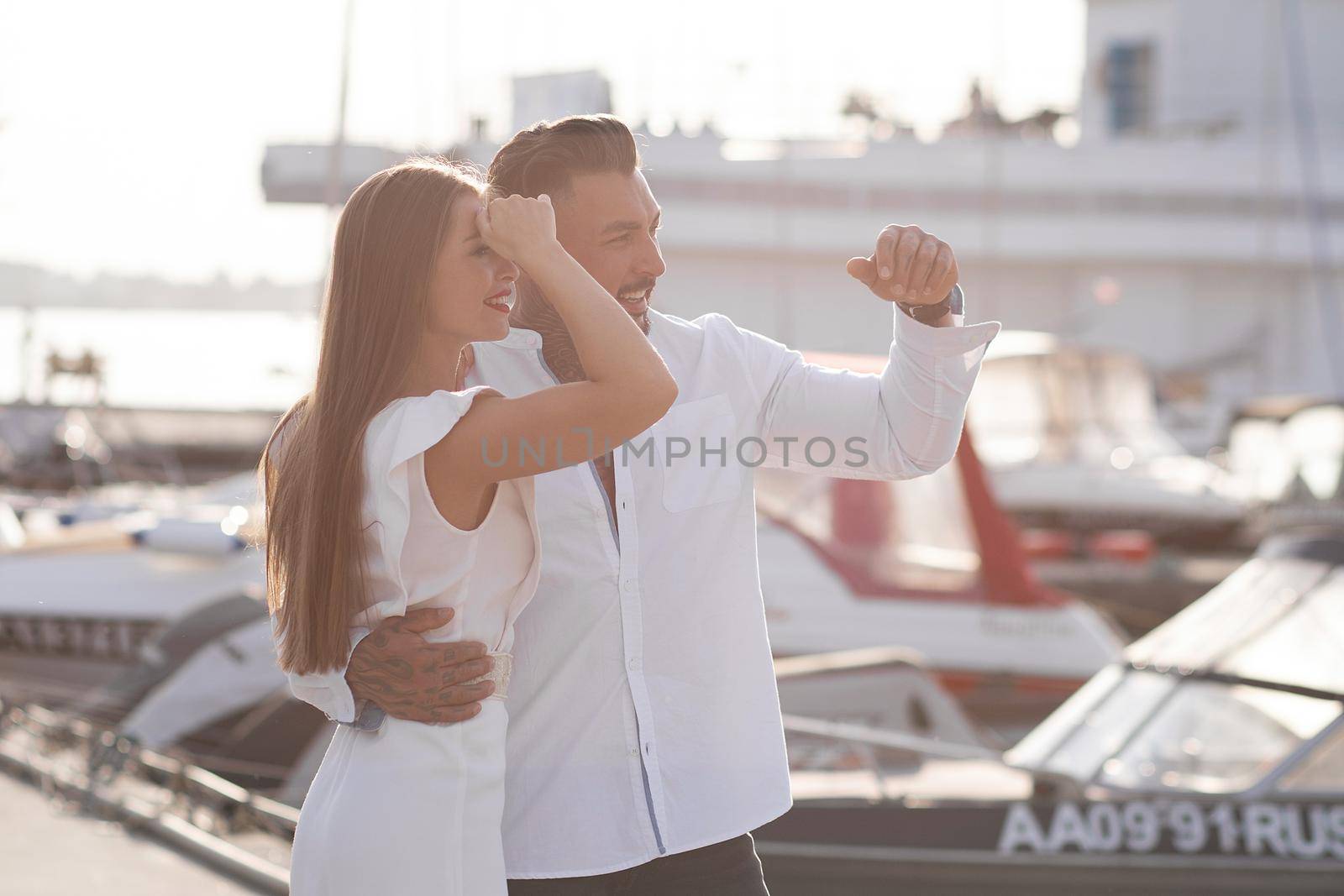 Loving couple hugging while standing on embankment near boats on sunny day in summer