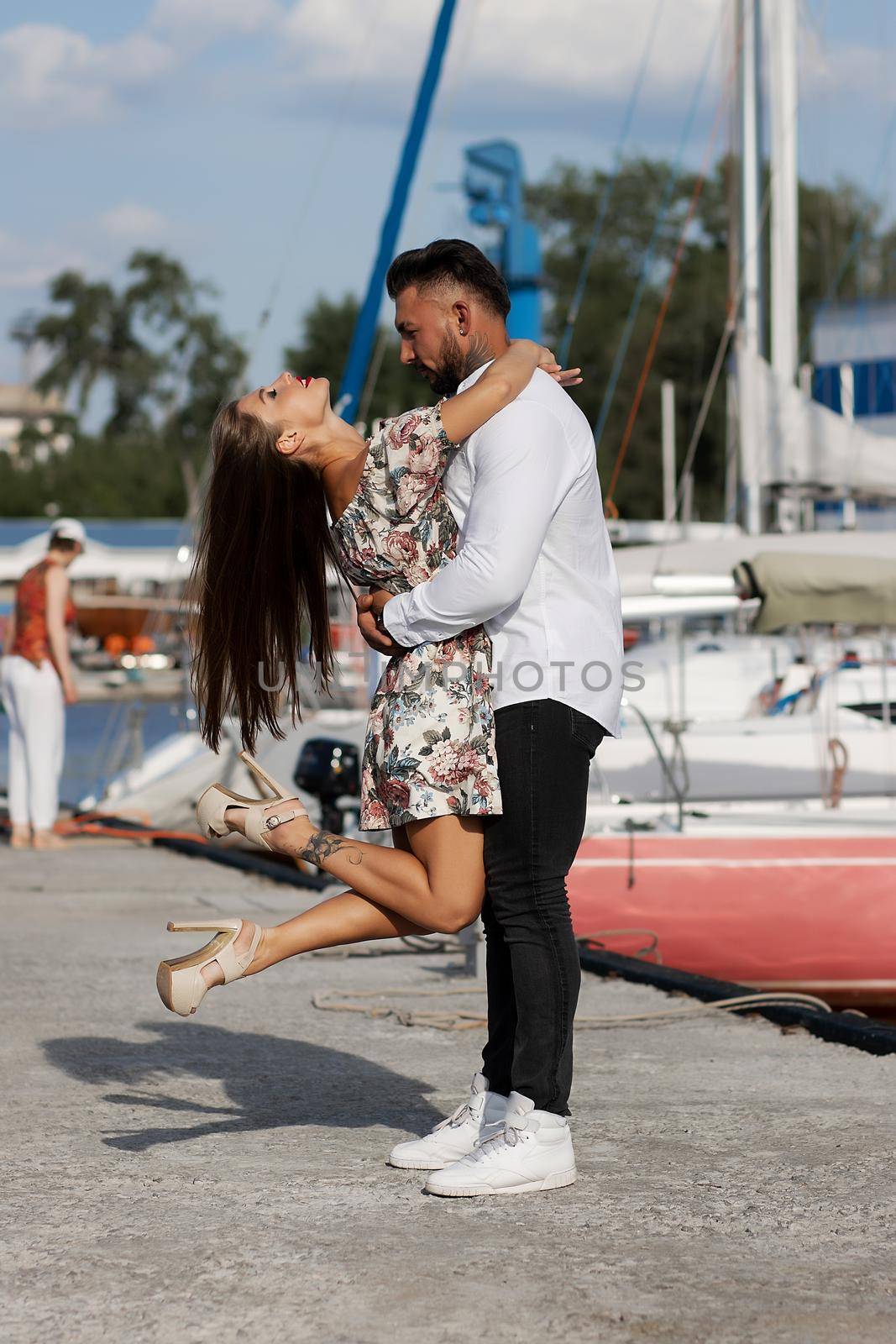 Side view of cheerful couple in love hugging in harbor with boats on sunny day in summer