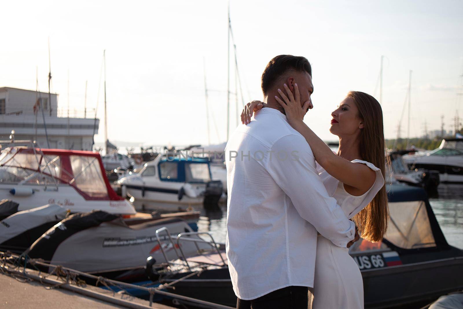 Loving couple hugging while standing on embankment near boats on sunny day in summer