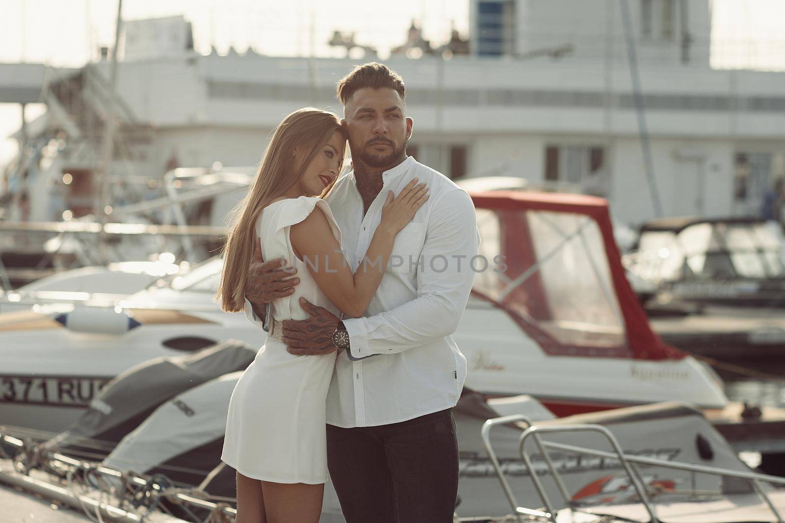 Loving couple hugging while standing on embankment near boats on sunny day in summer