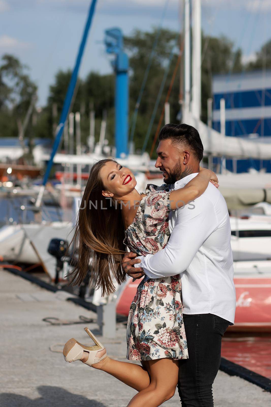 Side view of cheerful couple in love hugging in harbor with boats on sunny day in summer