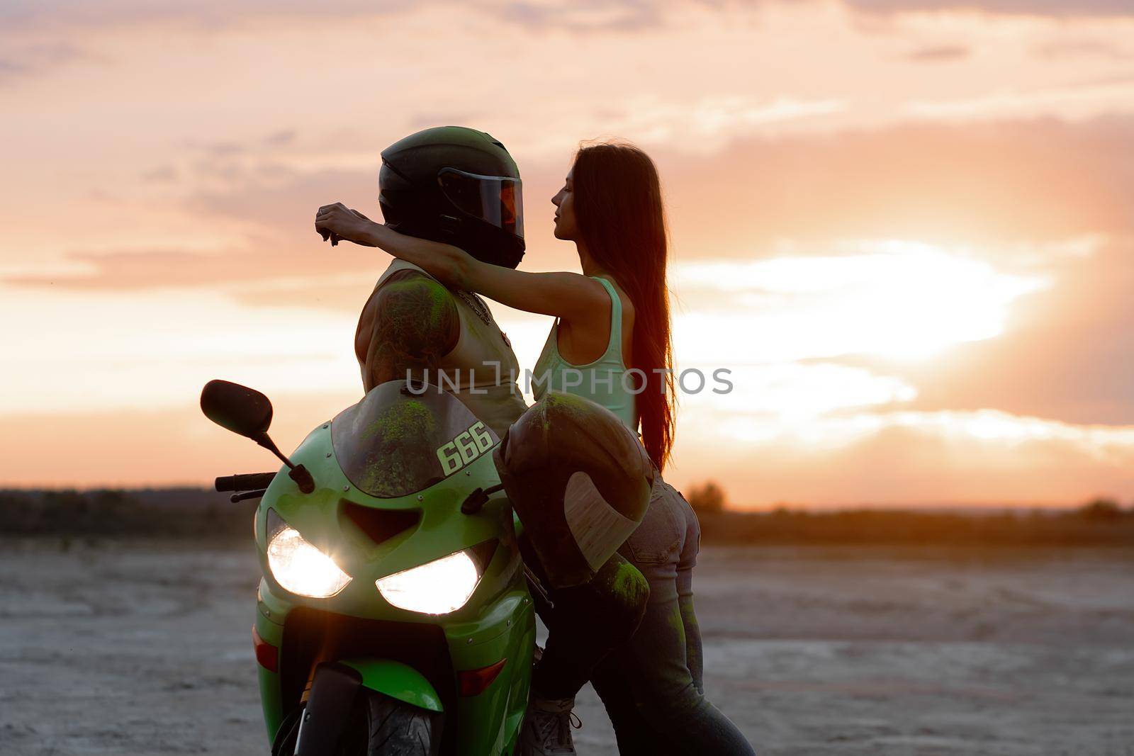 Side view of couple in love tenderly hugging near motorcycle parked on sandy seashore against sundown sky