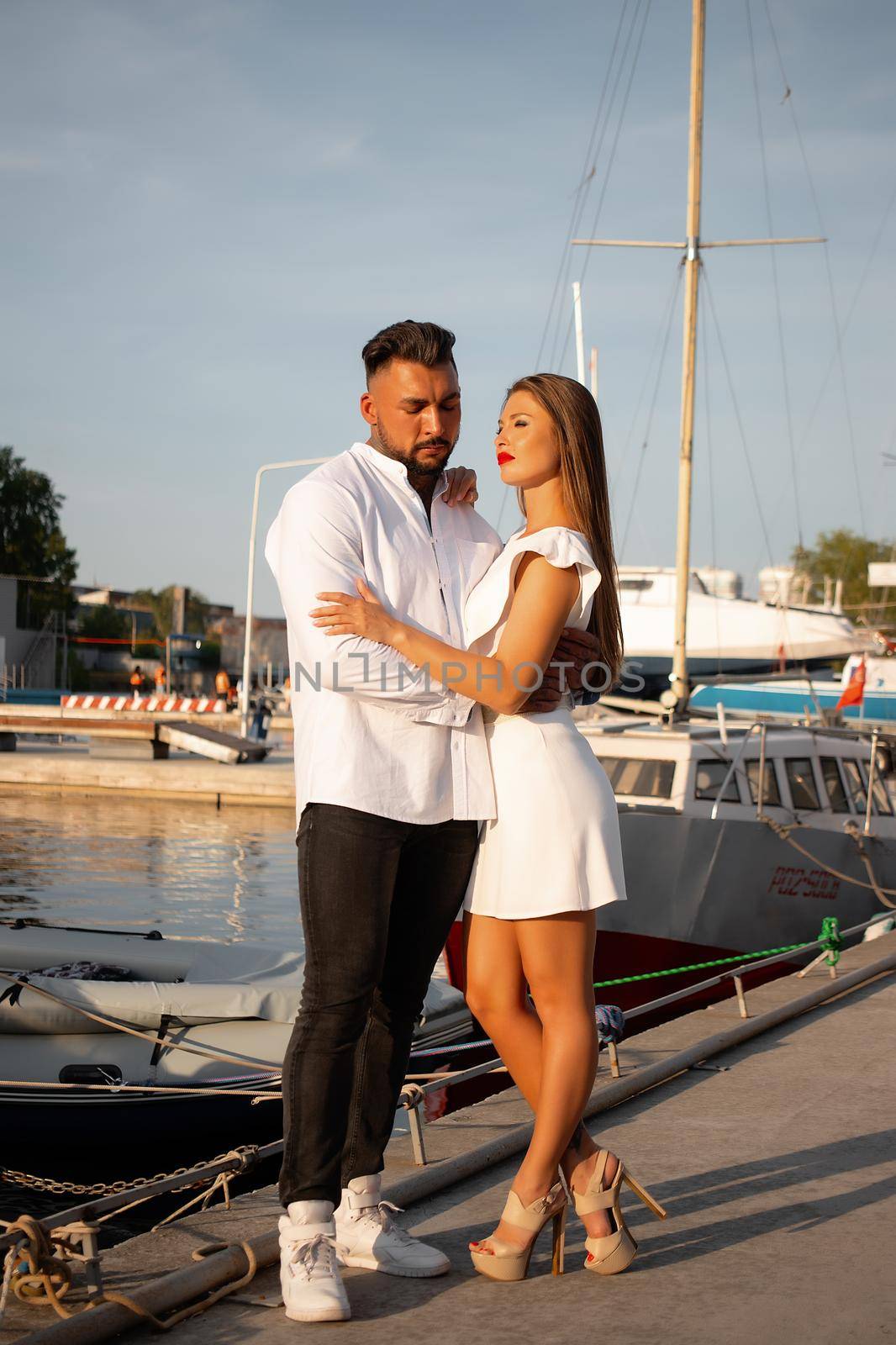 Loving couple hugging while standing on embankment near boats on sunny day in summer