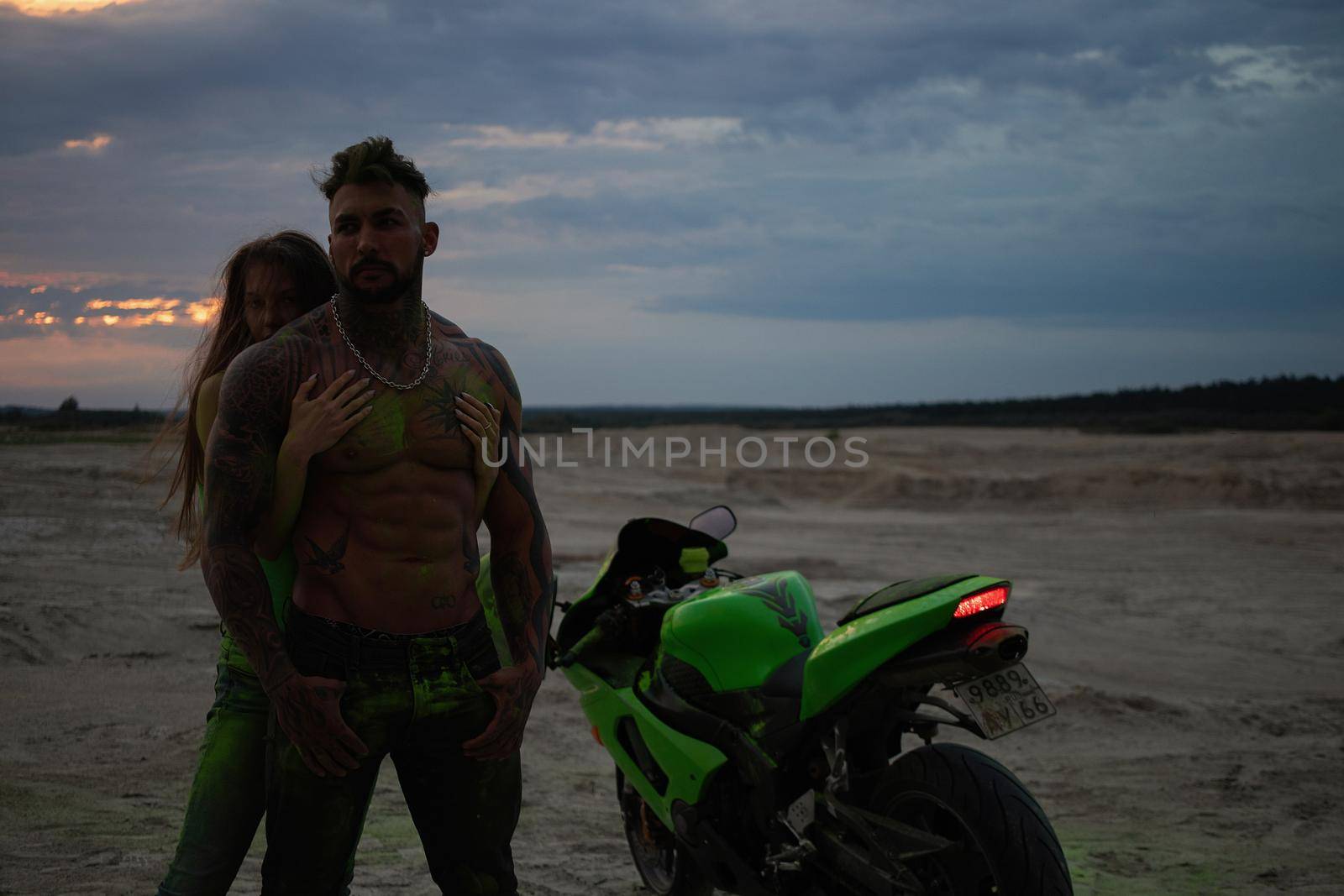 Couple embracing near motorbike on beach at sunset by 3KStudio