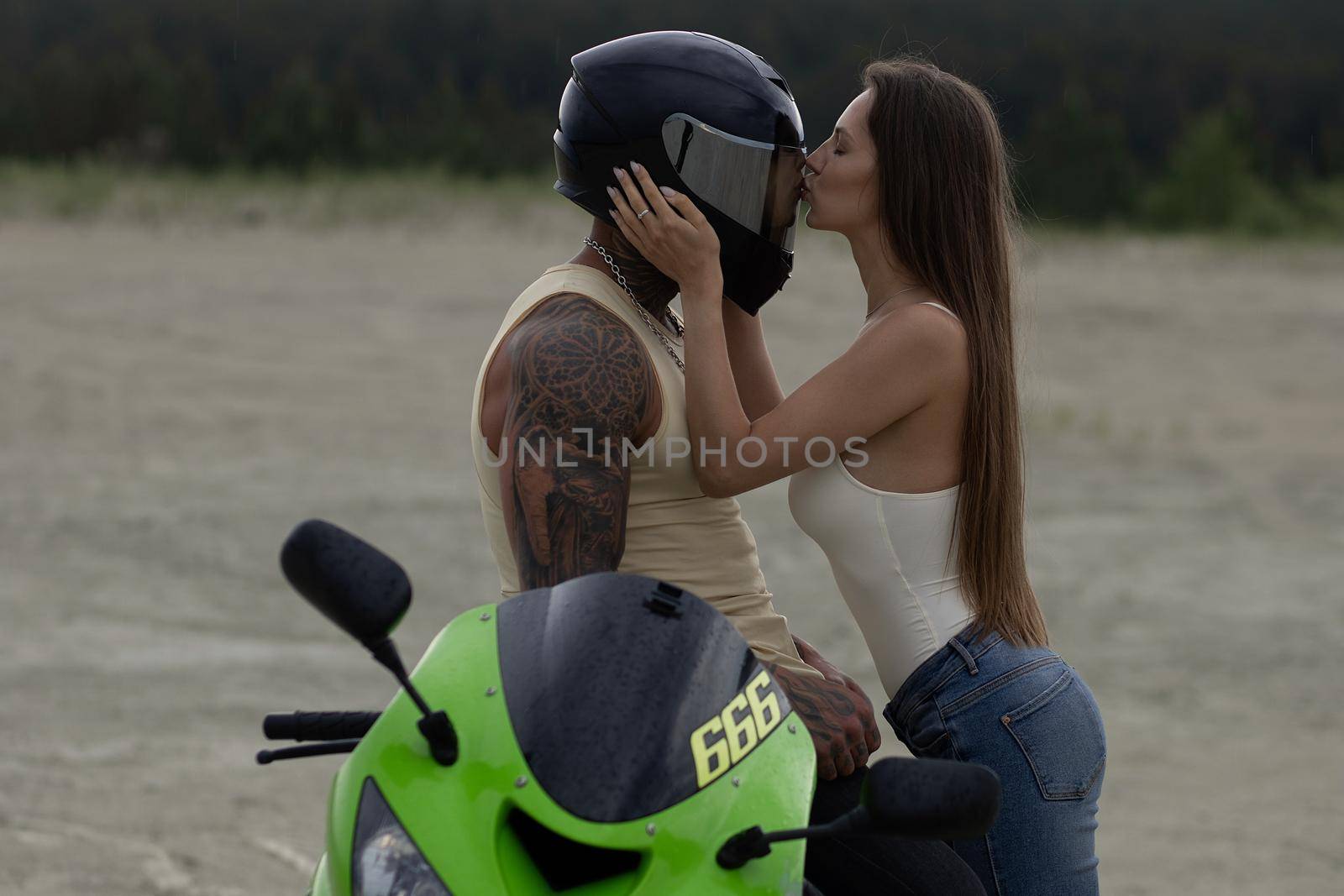 Side view of stylish loving couple cuddling near motorbike on beach at sunset