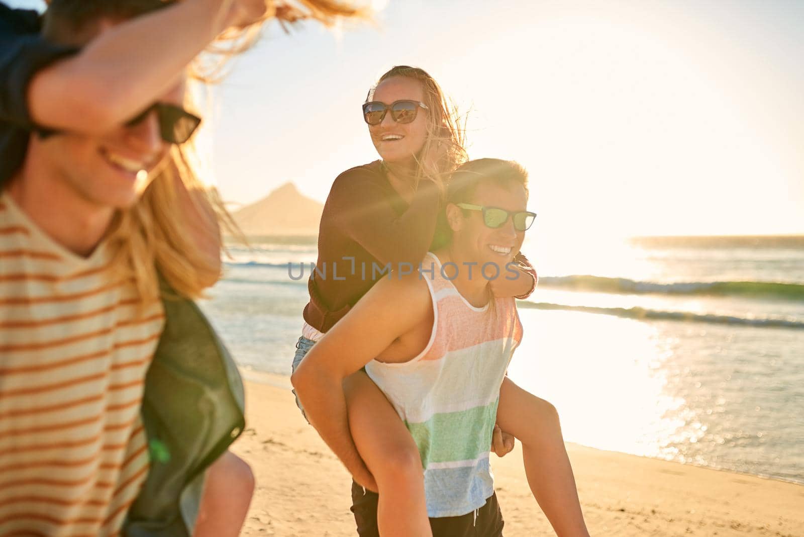 Cropped shot of two affectionate young men piggybacking their girlfriends at the beach.