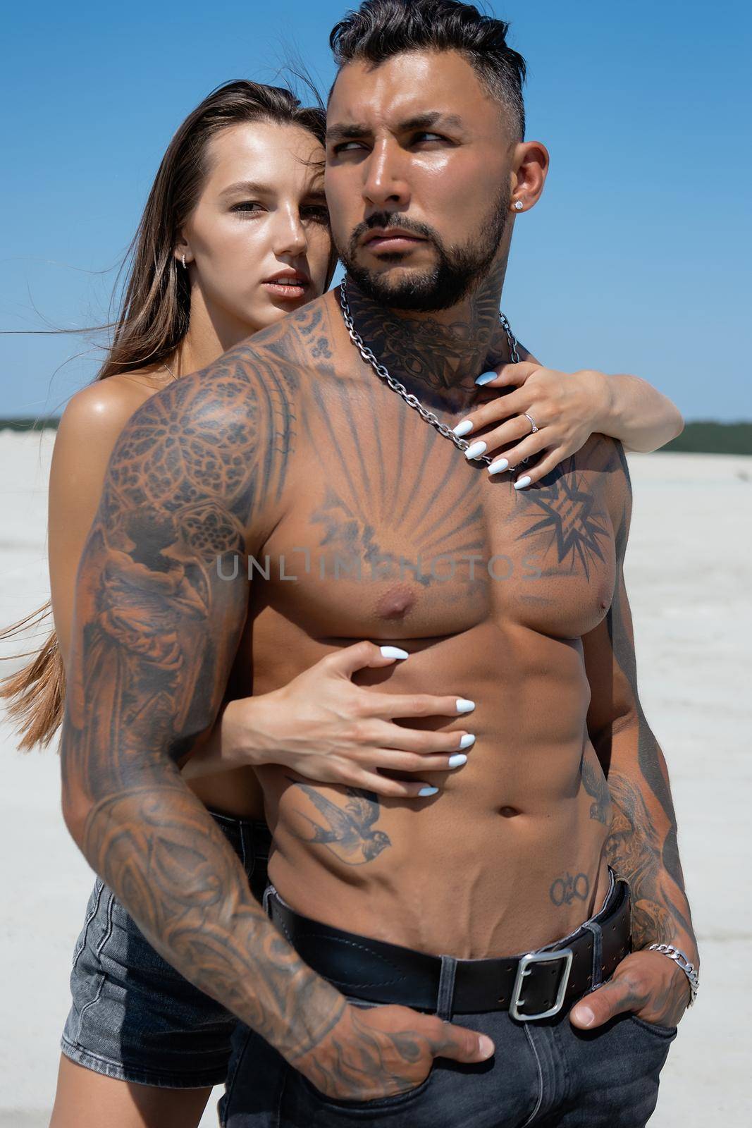 Seductive female in swimsuit and fit male with naked torso hugging while standing on sandy seashore on sunny day in summer