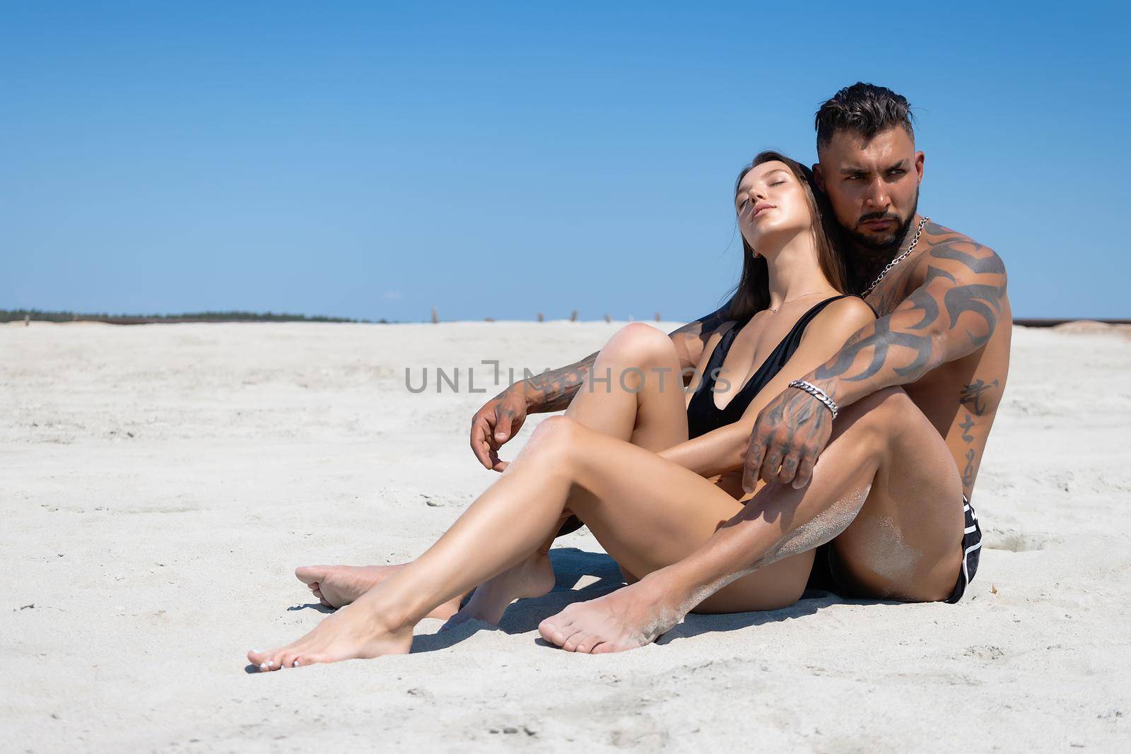 Side view of seductive woman in swimsuit looking at man lying on sandy beach in summer