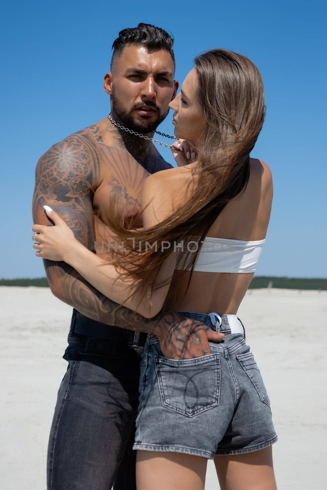 Seductive female in swimsuit and fit male with naked torso hugging while standing on sandy seashore on sunny day in summer