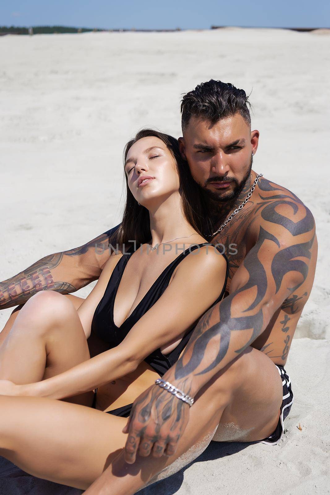 Side view of seductive woman in swimsuit looking at man lying on sandy beach in summer