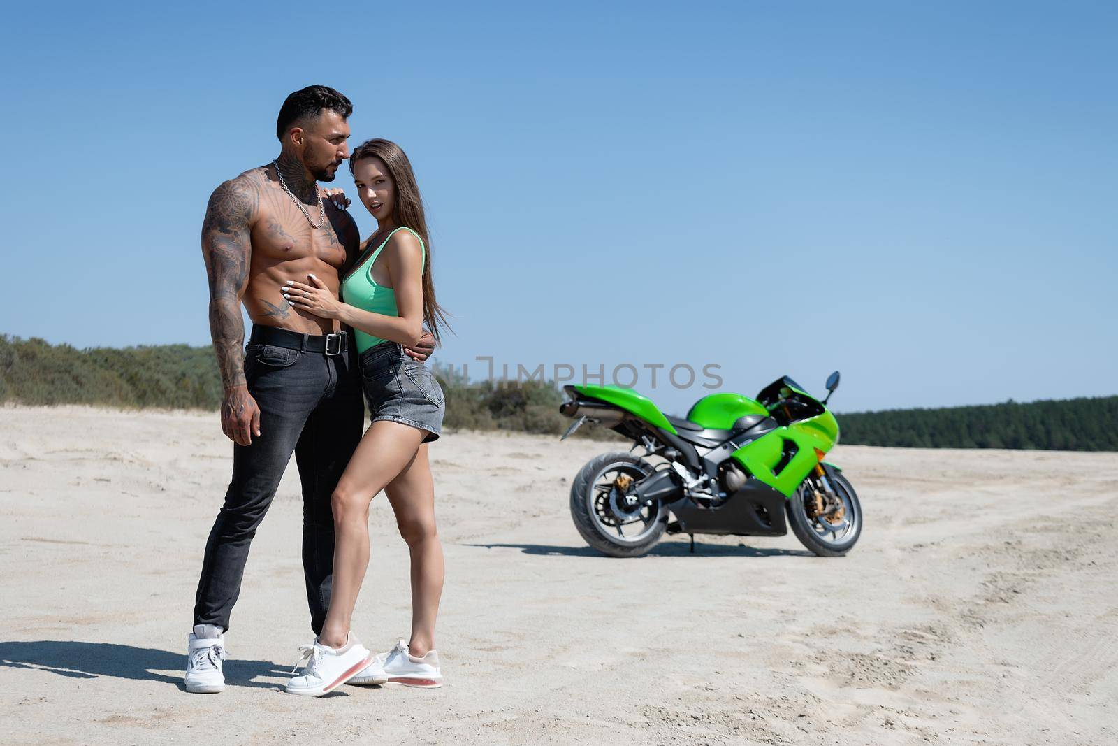 Confident man and young female standing and hugging against motorbike in countryside by 3KStudio