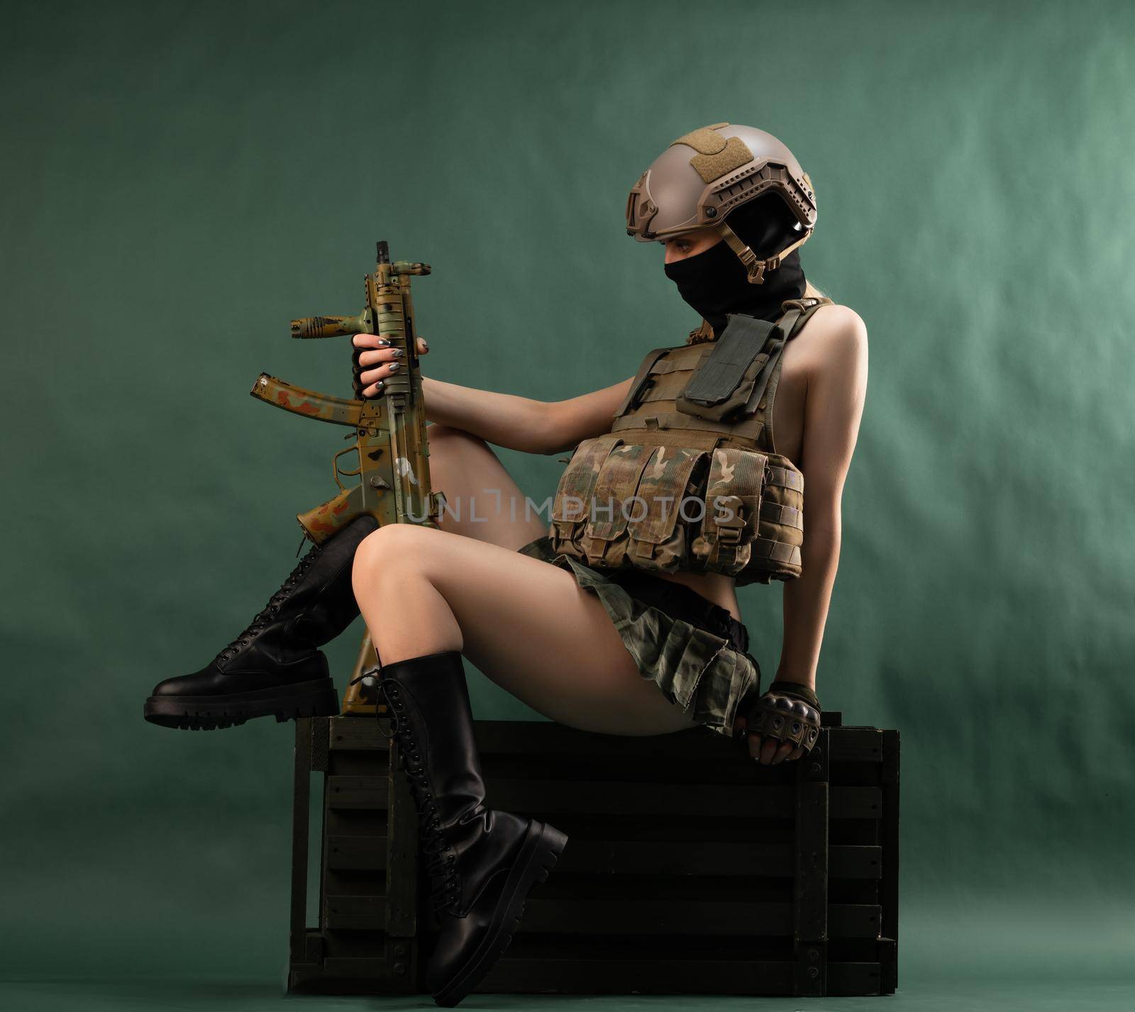 a girl soldier armed with an automatic rifle in military clothes sits on a gun case on a green background by Rotozey