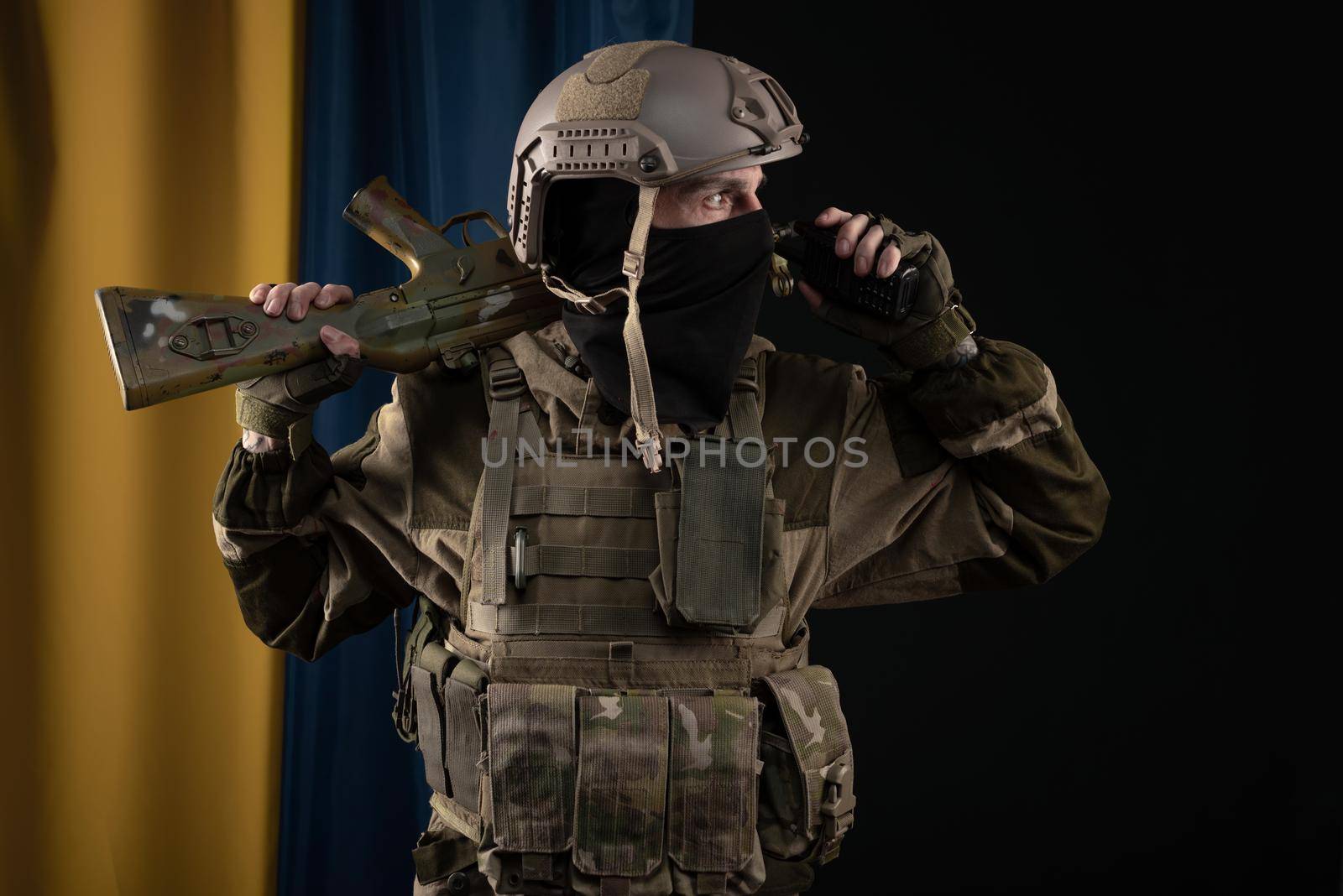 a male soldier in a military uniform and helmet with a weapon on the background of the national flag of Ukraine by Rotozey