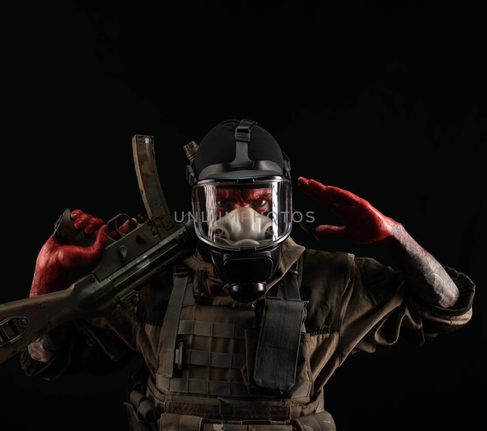 man in a military uniform and a gas mask holds a weapon with bloody hands with an angry expression of emotions