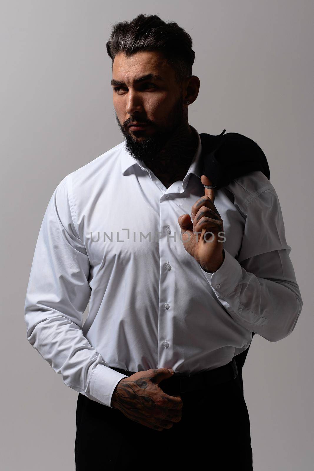 Bearded Hispanic guy in dark vest and white shirt with tie looking at camera with hands in pockets in studio