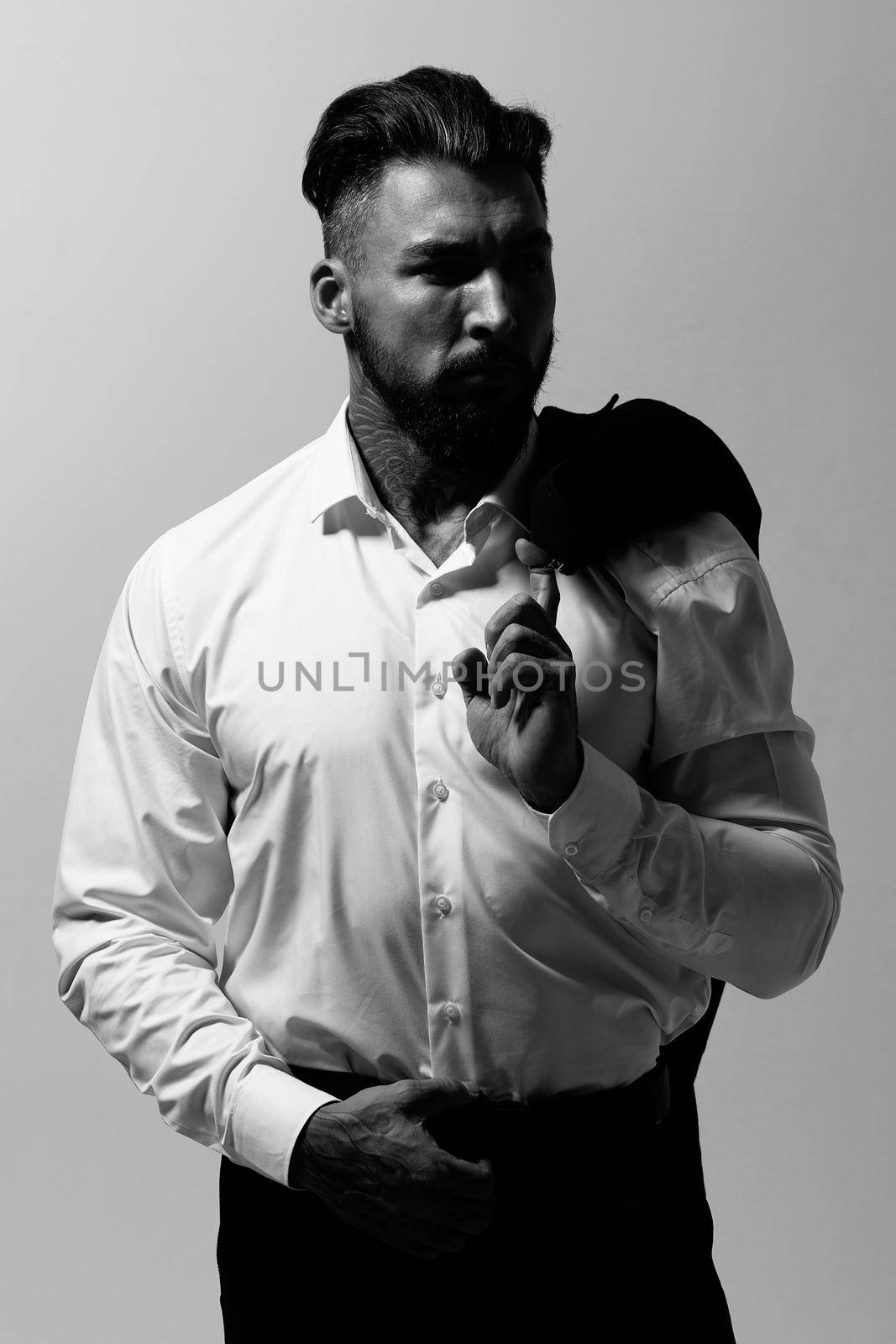 Bearded Hispanic guy in dark vest and white shirt with tie looking at camera with hands in pockets in studio