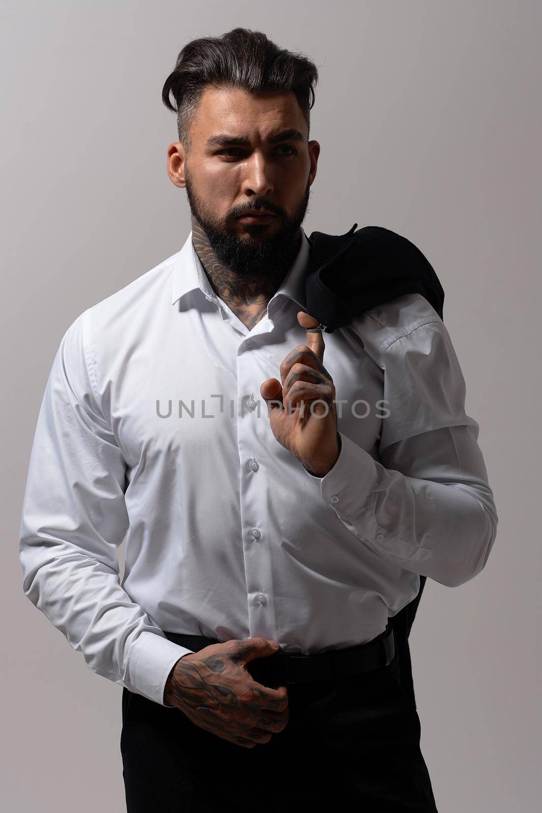 Bearded Hispanic guy in dark vest and white shirt with tie looking at camera with hands in pockets in studio