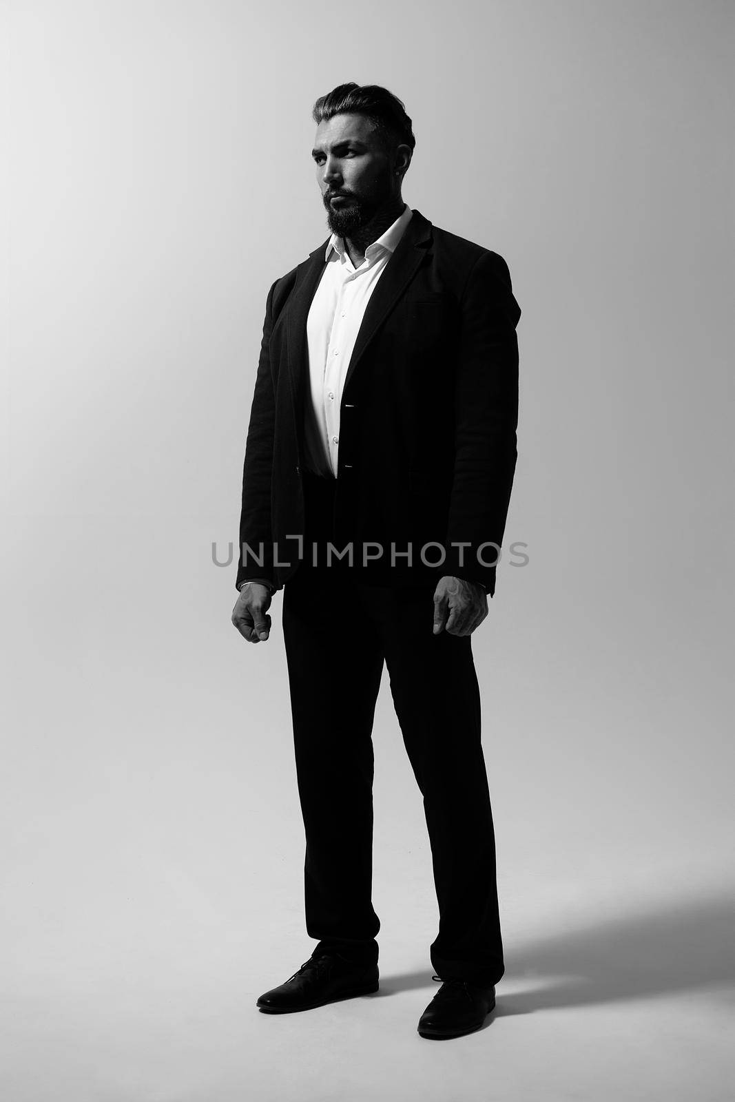 Bearded Hispanic guy in dark vest and white shirt with tie looking at camera with hands in pockets in studio