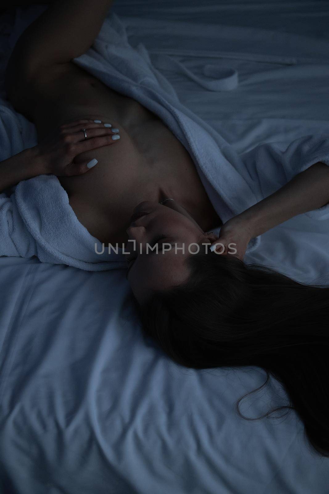 From above of topless sexy female in bathrobe lying on comfortable bed in bedroom